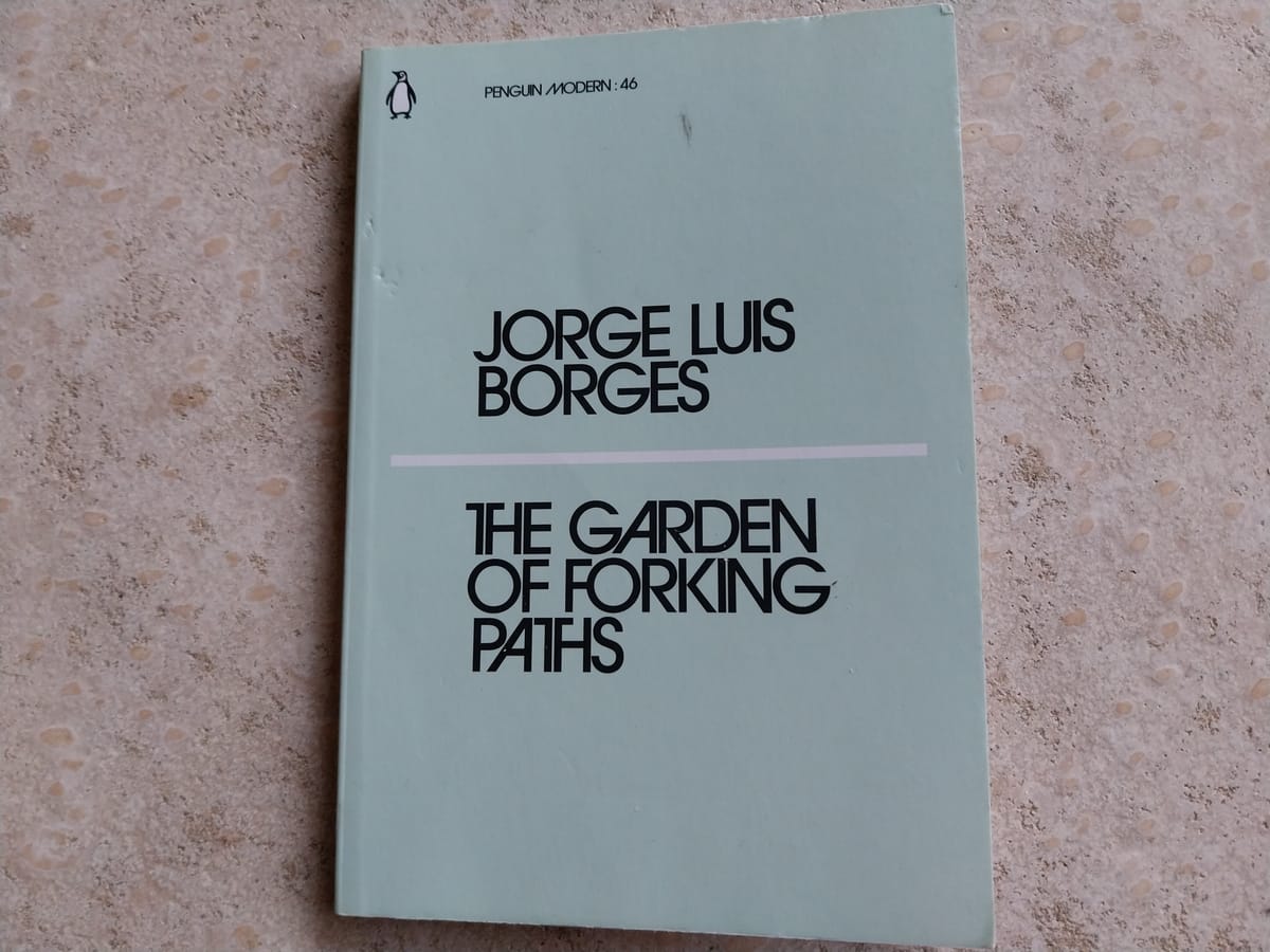 On a concrete background, a light-blue book. The book is The Garden of Forking Paths by Jorge Luis Borges.
