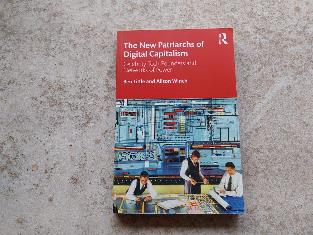 A book lying on a concrete surface. The book is partially red, partially occupied by an image of office workers in front of a large, old computer.