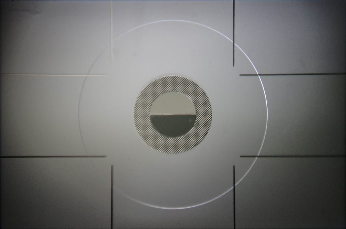 Image of a camera viewfinder without a lense. It is predominantly grey, and the centre of the image is occupied by a series of concentric circles.