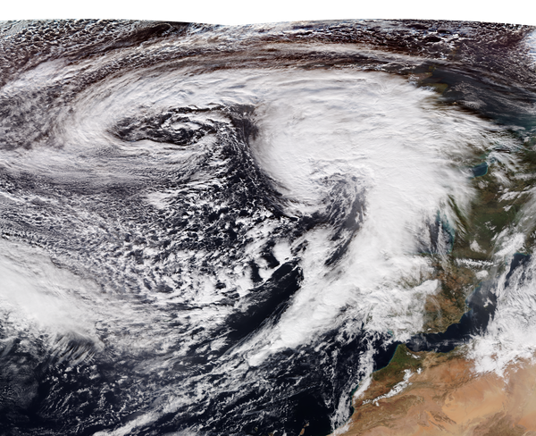 Overhead view of a storm, with clouds swirling in the foreground, and water and land in the background.