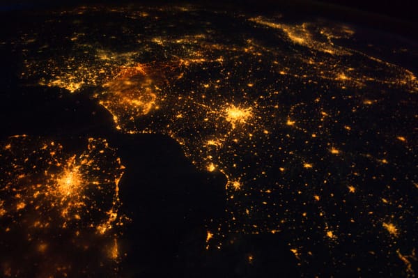 A mostly dark image of landmasses at night with spots of light where there are urban area. The patterns of lights look like networks.