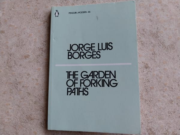 On a concrete background, a light-blue book. The book is The Garden of Forking Paths by Jorge Luis Borges.