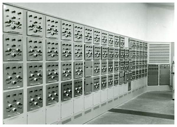 A black and white photo of a wall with a series of metal panels fitted into it. Each panel has several switches and buttons.