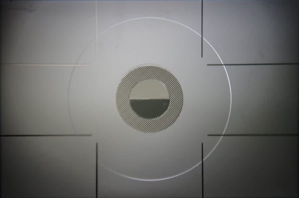 Image of a camera viewfinder without a lense. It is predominantly grey, and the centre of the image is occupied by a series of concentric circles.